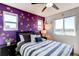 A bedroom with a striped bed, purple accent wall and ceiling fan at 10152 Southlawn Cir, Commerce City, CO 80022