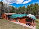 Exterior view of home with wood siding, green metal roof, and patio area in wooded setting at 9123 Booker Ln, Conifer, CO 80433