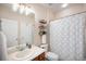 Neutral toned bathroom with a single sink vanity, toilet, shelving unit, and a blue leaf patterned shower curtain at 6092 S Ouray St, Aurora, CO 80016