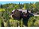 Stunning aerial view of wood cabin surrounded by trees, showcasing large windows and an expansive deck at 10333 Georgia Cir, Morrison, CO 80465