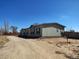 View of home with light-green siding and black trim, gravel driveway, and a spacious yard with blue skies at 15460 Casler Ave, Fort Lupton, CO 80136