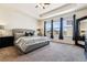 Bright main bedroom with large windows, a tray ceiling, neutral carpet, and a comfortable upholstered bed at 16201 Lanceleaf Pl, Parker, CO 80134