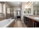 Bright bathroom featuring a tub, shower, and a double sink with dark cabinets in a neutral color palette at 10221 Nucla St, Commerce City, CO 80022
