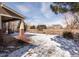 A winter view of the backyard, featuring brick accents, a partially covered porch and distant neighboring houses at 17853 W 77Th Ln, Arvada, CO 80007