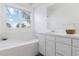 Bright bathroom featuring a soaking tub under a large window, white cabinets and plenty of counter space at 10843 W Hinsdale Dr, Littleton, CO 80127