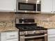 A stainless steel gas range with overhead microwave complements the granite countertops and tile backsplash at 7400 W Grant Ranch Blvd # 19, Littleton, CO 80123