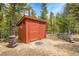 Exterior of a red outbuilding with a wood-burning stove and stacked firewood, nestled among tall trees at 387 Pine Dr, Idaho Springs, CO 80452