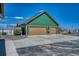 Three-car garage with tan doors, green siding, and a concrete driveway under a bright blue sky at 55610 E 40Th Ave, Strasburg, CO 80136