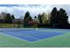 View of a blue and green outdoor tennis court surrounded by mature trees with a dark-colored net and green fencing at 6719 E Costilla Cir, Centennial, CO 80112