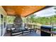 Outdoor living area with stone fireplace, wood ceiling, seating and grill overlooking the treed yard at 18376 Heavens Pl, Monument, CO 80132