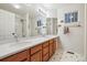 Bright bathroom with dual sinks, white countertops, wood cabinets, and a shower at 9478 Burgundy Cir, Highlands Ranch, CO 80126