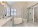 Bright bathroom featuring a glass shower, soaking tub, marble floors and counters, and white cabinets at 286 Warwick Pl, Castle Pines, CO 80108
