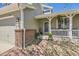 View of the front porch with brick columns and a white railing, accompanied by lush greenery and stone landscaping at 1153 Berganot Trl, Castle Pines, CO 80108