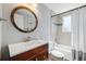 Updated bathroom with modern fixtures, cherry vanity, round mirror, and tiled shower/tub combo at 7350 W 21St Ave, Lakewood, CO 80214