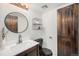Stylish half-bathroom with vanity, round mirror, and unique wood door at 7705 W 87Th Dr, Arvada, CO 80005
