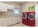 A spacious laundry room featuring white cabinets, a sink, a window, and modern red washer and dryer machines at 3358 Castle Butte Dr, Castle Rock, CO 80109