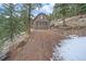 Two-car brown garage with a centered window on a gravel driveway surrounded by forest and snow at 6080 Kilimanjaro Dr, Evergreen, CO 80439