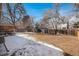 Wide backyard with a wooden fence, trees, and minimal grass covered in patchy snow and brown leaves at 3083 S Xanthia St, Denver, CO 80231
