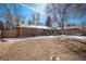 Large backyard featuring a brick house, a deck with chairs, bare trees, and a partially snow-covered lawn at 3083 S Xanthia St, Denver, CO 80231