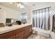 Bathroom features a dual sink vanity, a shower-tub combo with a curtain and neutral tile at 15056 Fillmore Way, Thornton, CO 80602