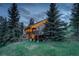 Exterior view of the home with lit balconies surrounded by mature trees at twilight at 96 Carolyn Rd, Evergreen, CO 80439