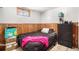 Cozy bedroom with wood paneled walls, wood-look flooring, a black dresser and a queen bed at 7066 Jennie Dr, Denver, CO 80221
