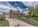 A brick house with a detached garage, and a driveway is complemented by green lawns and blue skies at 1334 Xavier St, Denver, CO 80204