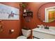 Decorated powder room featuring a white sink, round mirror, decorative wall art, and burnt orange walls at 5671 Raleigh Cir, Castle Rock, CO 80104
