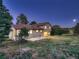 Large backyard with mature trees and lush lawn at dusk, illuminated by lights shining from the house at 8916 Sunridge Hollow Rd, Parker, CO 80134