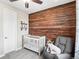 Cozy Bedroom with a rustic wood accent wall, crib, gray rocking chair, and soft carpet at 3745 Spanish Oaks Trl, Castle Rock, CO 80108