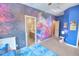 Themed bedroom with vibrant galaxy wallpaper, adjoining bathroom, and bright blue rug at 735 Woodmoor Acres Dr, Monument, CO 80132