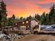 Beautiful home exterior against a vibrant sunset sky with a stone wall and surrounded by a lush forest landscape at 28268 Shadow Mountain Dr, Conifer, CO 80433