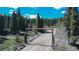 Rustic log entryway to a mountain property leading to a dirt road surrounded by lush forest and blue sky at 297 Robertson Ln, Breckenridge, CO 80424