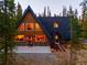 A-frame home with wood and dark gray accents, surrounded by tall evergreen trees and concrete patio at 297 Robertson Ln, Breckenridge, CO 80424