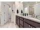 Bathroom featuring granite counters, dual sinks, dark cabinets, large mirror and door leading to the tiled walk-in shower at 17520 E 95Th Pl, Commerce City, CO 80022