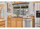 Close-up of the kitchen sink area featuring wood cabinets, stainless steel dishwasher, and a large window at 8468 Chase Dr, Arvada, CO 80003
