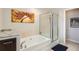 Bright bathroom featuring a soaking tub with glass door enclosure, tiled walls, and decorative art at 8300 Fairmount Dr # Aa102, Denver, CO 80247