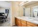 Bathroom with double vanity, wooden cabinets, and an adjacent room with a workspace and natural light at 11830 Snowshoe Dr, Parker, CO 80138