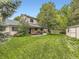 Expansive backyard featuring a well-maintained lawn, mature trees, storage shed, and a covered patio area at 3210 S Espana Cir, Aurora, CO 80013