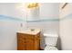 Bathroom featuring a wood vanity cabinet, white toilet, framed mirror, and blue decorative wallpaper at 6185 Sheridan Blvd, Arvada, CO 80003