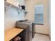 A modern laundry room with stainless steel washer and dryer, bright window, and shelving at 6883 E 132Nd Pl, Thornton, CO 80602