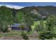 View of a well-maintained garage and verdant landscape backed by scenic hillside greenery and white fencing at 97 Soda Creek Rd, Evergreen, CO 80439
