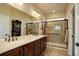 Bathroom with dual sinks, a glass-enclosed shower, and neutral tile floors, plus an open walk-in closet at 8255 E 150Th Pl, Thornton, CO 80602