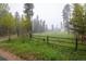 Spacious front yard with a black rail fence, tall trees, and green grass at 1194 Camp Eden Rd, Golden, CO 80403