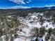 Stunning aerial view shows a snow-covered landscape, showcasing a home and rolling hills covered in trees at 20101 Spring Gulch Rd, Morrison, CO 80465