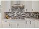 Close up of the stove top with stylish backsplash, stainless hood and white cabinets at 11400 W Grand Ave, Littleton, CO 80127