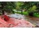 Red Adirondack chairs sit riverside on this home's lovely stone patio at 4230 S Meadow Brook Ln, Evergreen, CO 80439