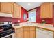 Cozy kitchen featuring wood cabinets, neutral countertops, and a bright red accent wall at 7725 Hummingbird Green # 78, Frederick, CO 80530