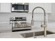 Close-up of a modern kitchen faucet, stainless steel appliances, and white countertops at 6153 N Ceylon St # 302, Denver, CO 80249