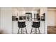 A stylish kitchen featuring black bar stools, modern appliances, and sleek white cabinetry with stone countertops at 10785 W 63Rd Pl # 108, Arvada, CO 80004